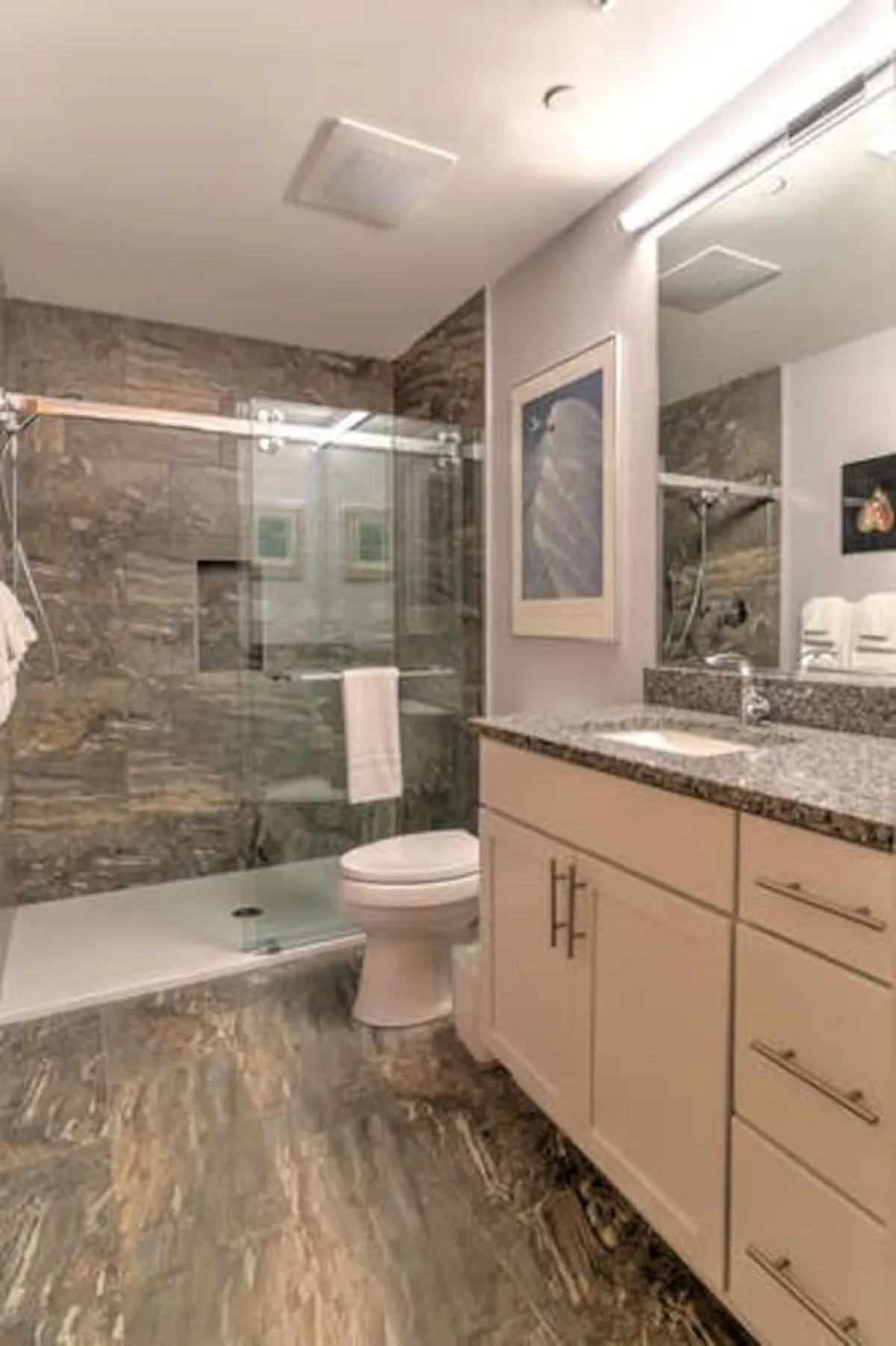 A sophisticated bathroom featuring a glass shower enclosure, granite countertop, modern fixtures, and decorative artwork. The space feels spa-like, inviting moments of relaxation and refreshment after a busy day.