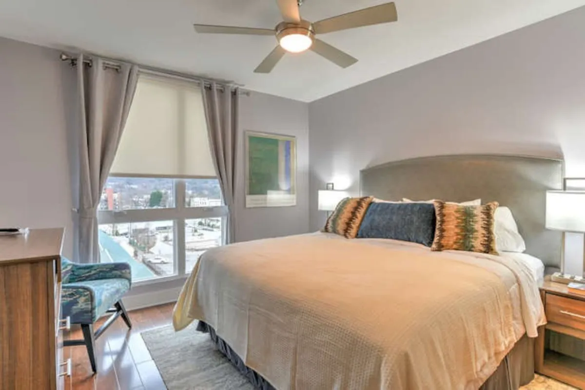 A tranquil bedroom scene featuring a comfortable bed adorned with soft linens, tasteful artwork above the headboard, a window offering gentle natural light, a dresser, and a cozy chair in the corner. The room radiates a peaceful, restorative atmosphere ideal for unwinding.