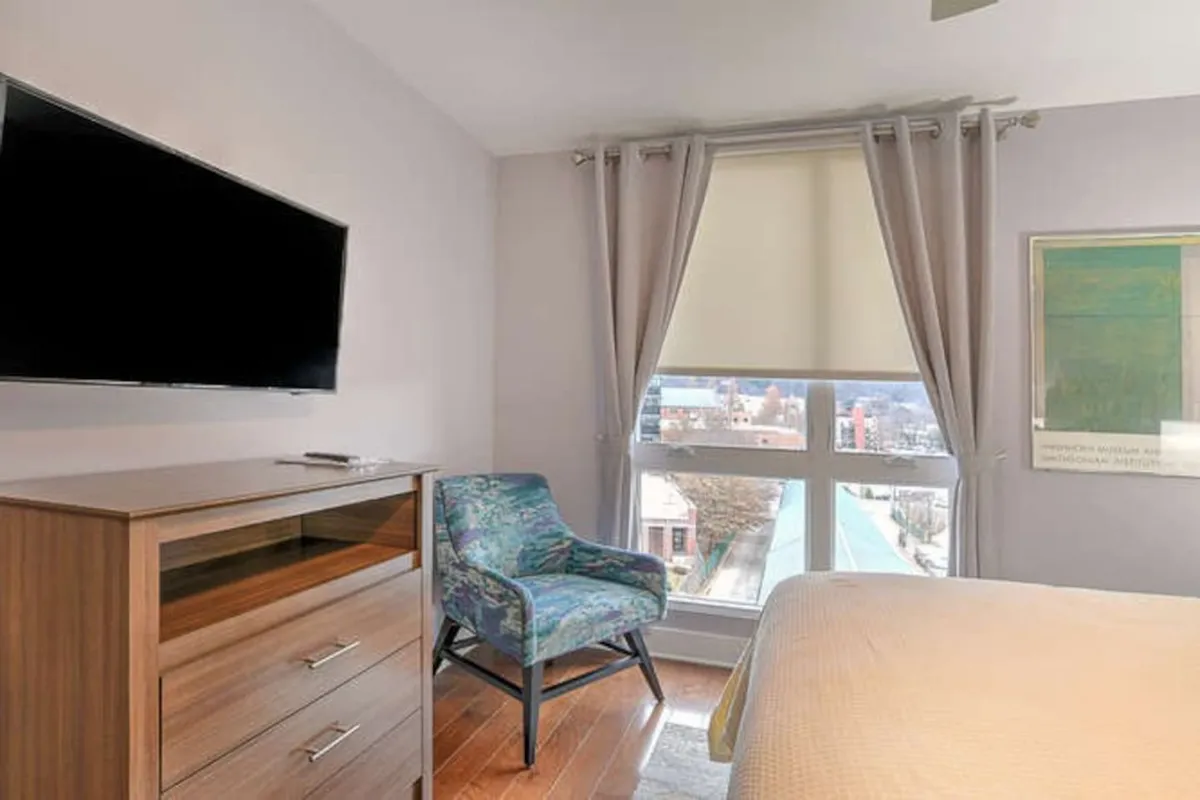 A cozy living room nook with a plush armchair, television, window view, and chest of drawers. This inviting corner is set up for relaxing, movie nights, or casual downtime, with natural light streaming in and a warm, homey vibe.