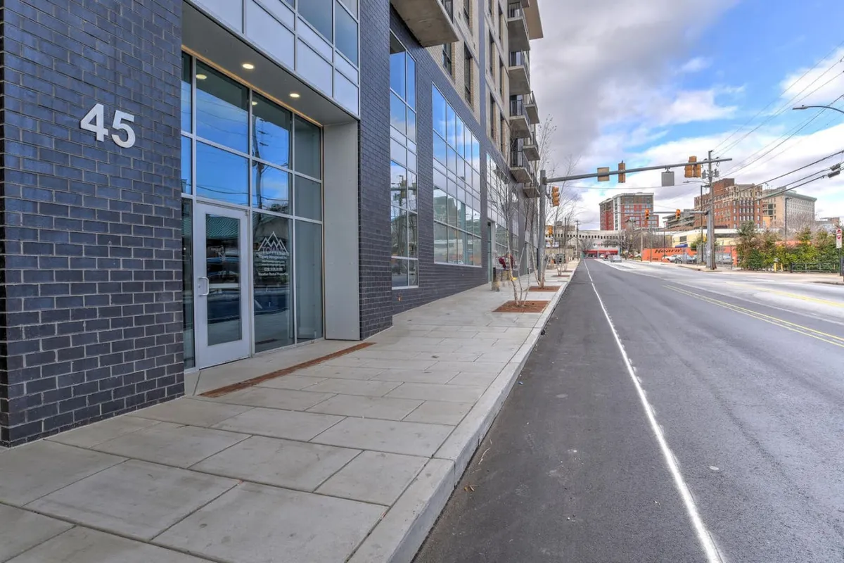 The exterior entrance of the building is showcased in this photo, with striking glass windows, the number '45' prominently displayed, and hints of bustling urban activity. The entrance is modern, clean, and signals a secure, exclusive entryway.