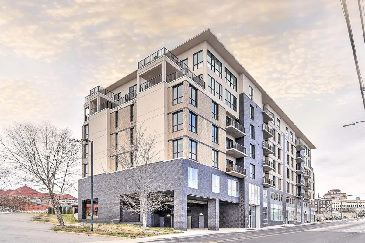 A modern exterior view of the building highlights its architectural design, expansive balconies, and large windows. The image suggests exclusivity and security while situating the property within a vibrant urban setting.