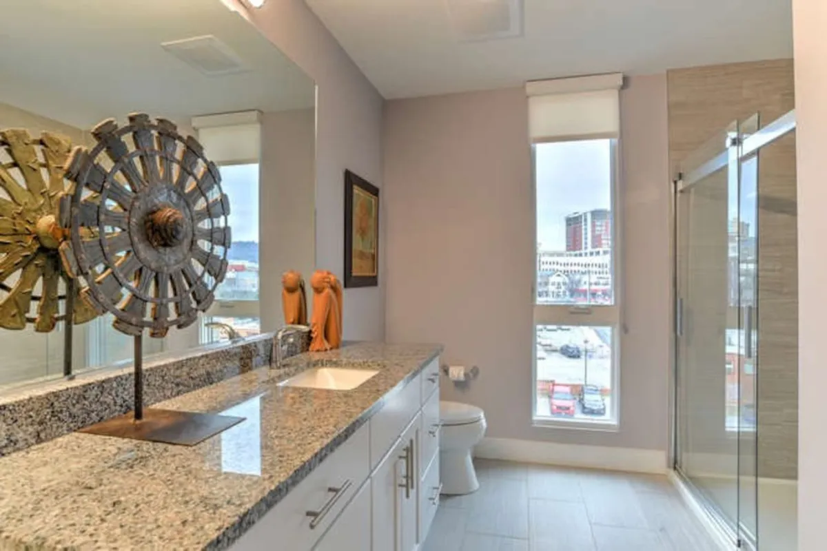 A contemporary bathroom with a granite countertop, decorative metal sculpture, large mirror, and a spacious shower enclosure. The space exudes a serene, spa-like ambiance—perfect for relaxation and personal grooming after a day out.